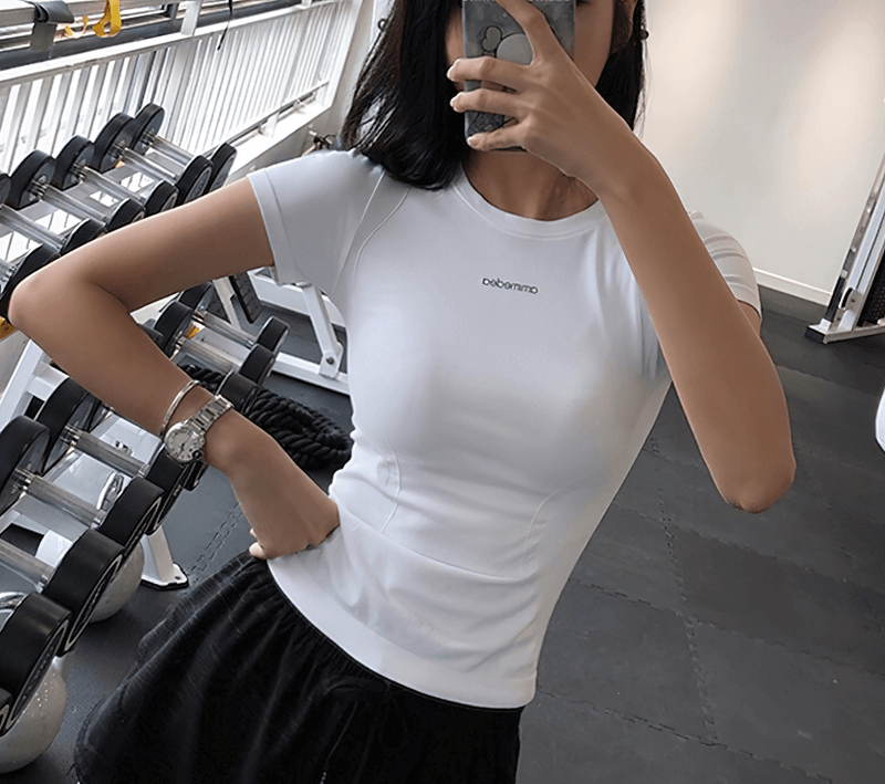 Woman wearing white fitness female breathable t-shirt for running, showcasing short sleeves in a gym setting.